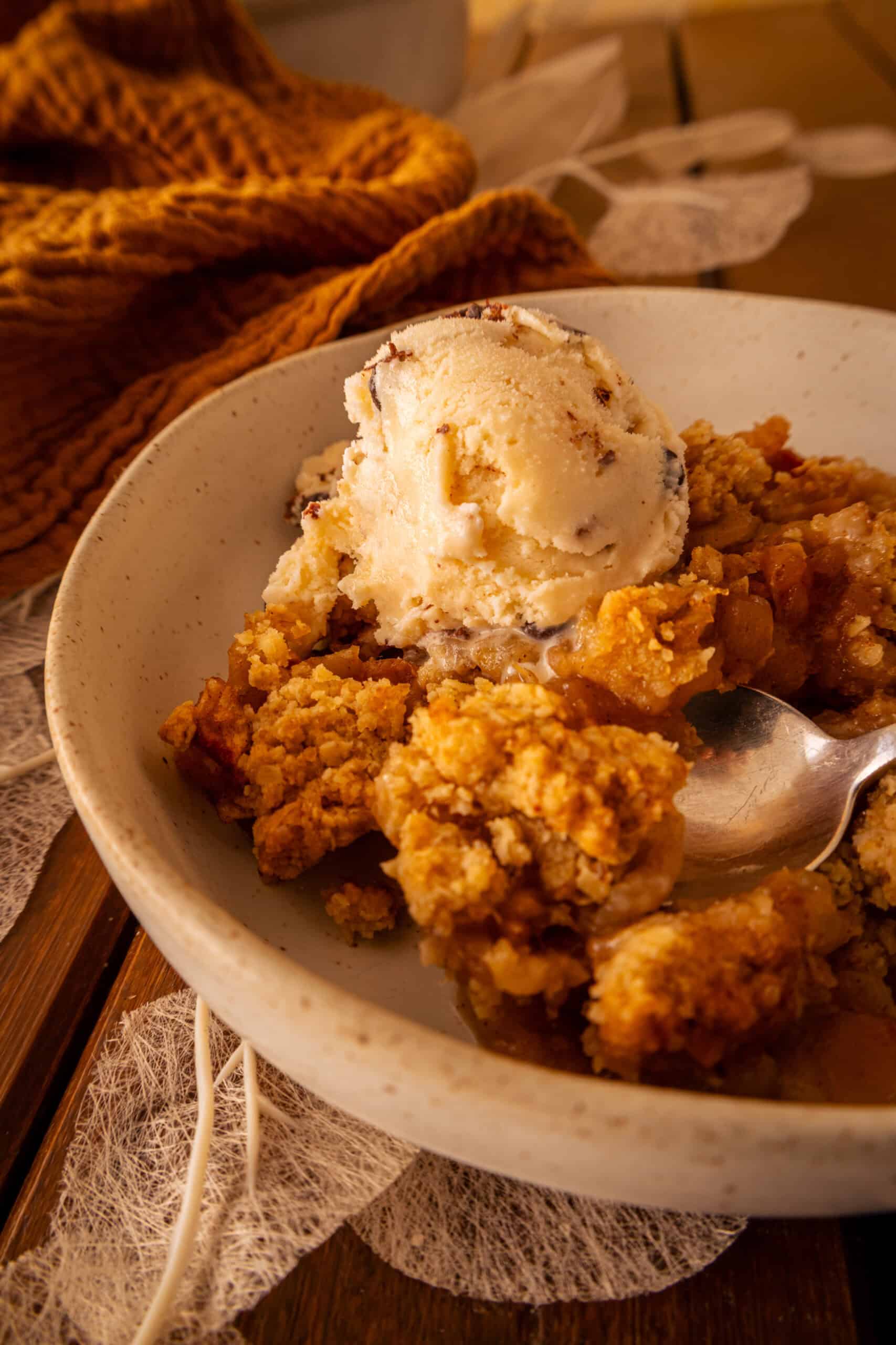 Apple Crumble mit Haferflocken und Vanilleeis auf rustikalem Holztisch, herbstliche Stimmung